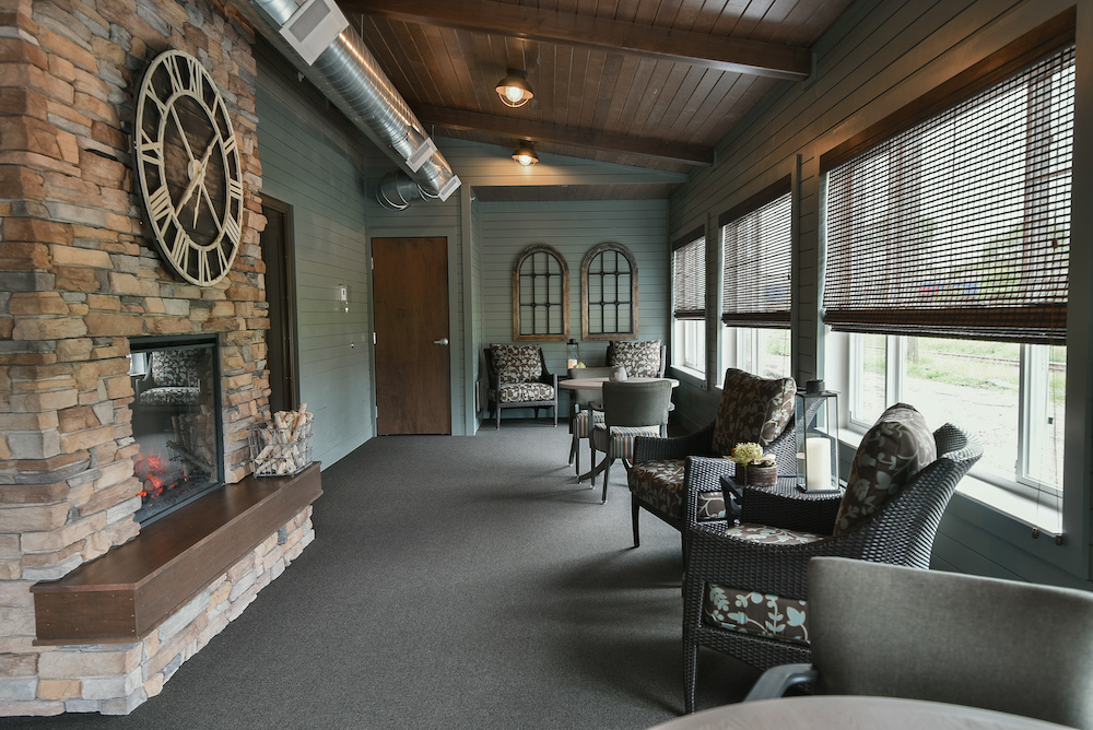 Cozy sunroom with wicker chairs, large stone fireplace, and rustic decor including a wall clock