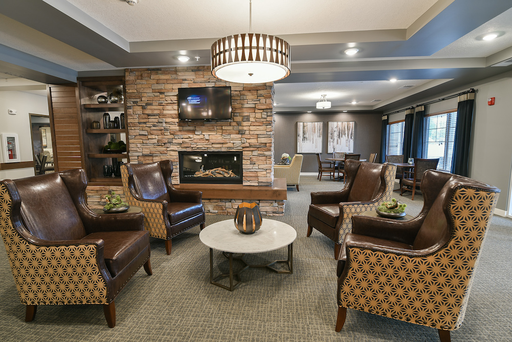 Cozy lounge with brown leather chairs, coffee table, stone fireplace, and modern lighting fixture