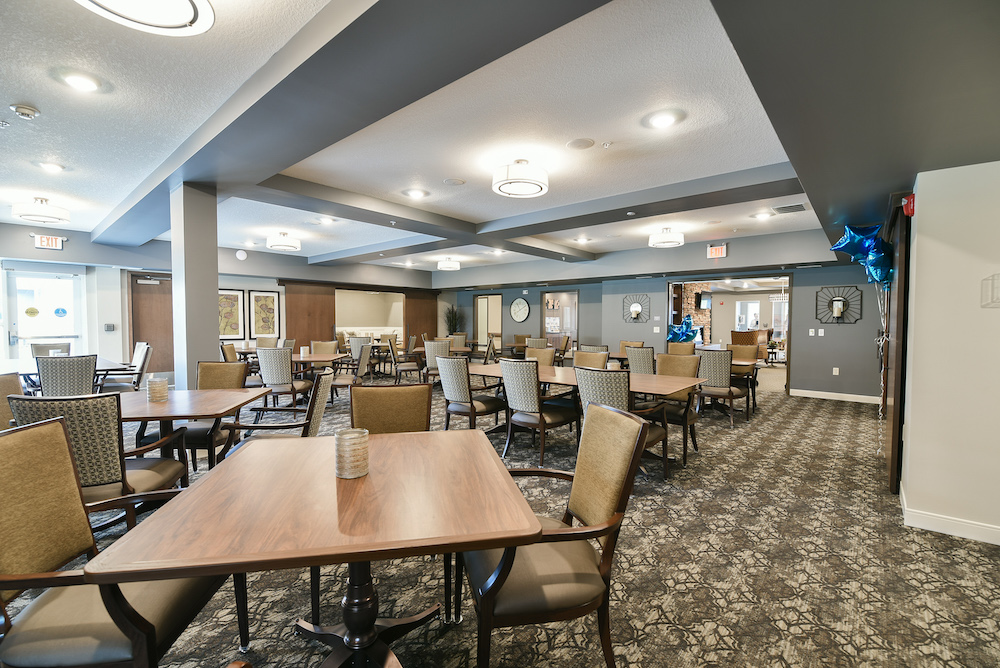 Dining room with multiple tables and chairs, modern lighting, and a patterned carpeted floor.