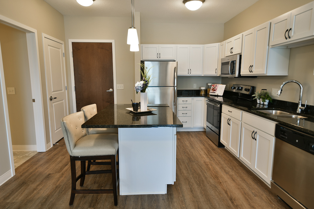 Modern kitchen with stainless steel appliances, white cabinets, and a central island with dining stools.