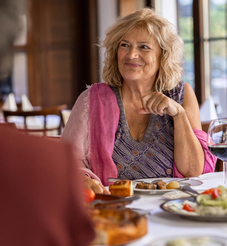 senior-friends-eating Senior woman enjoying a meal with friends at a restaurant, smiling and looking engaged.