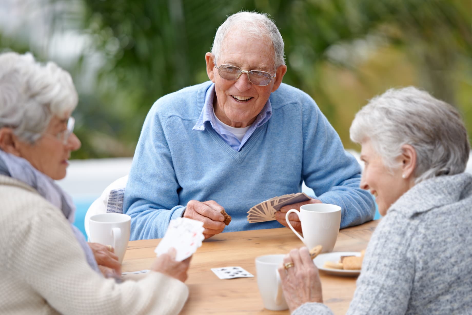 senior-man-and-friends-playing-cards-outdoors Two older adult women and a senior man smile while playing cards together